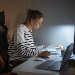 Estudiante estudiando por la noche con apuntes y ordenador