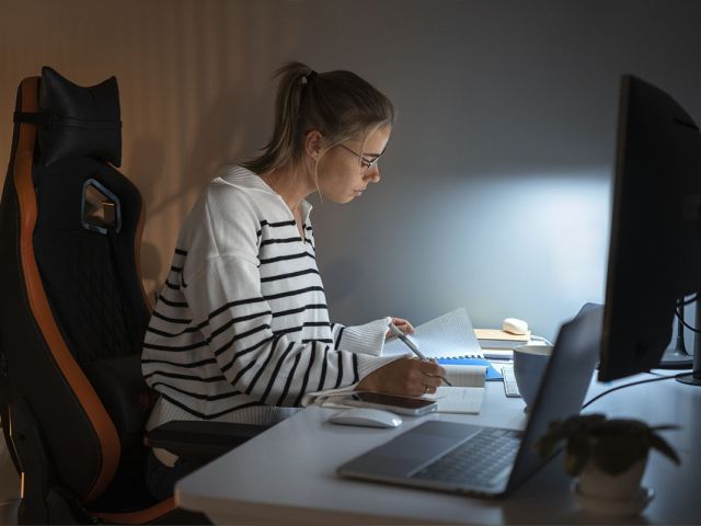 Estudiante estudiando por la noche con apuntes y ordenador